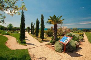 A well-maintained garden with a gravel path, various shrubs, and tall trees. - Mobile home with air conditioning, terrace and pool (Umag)