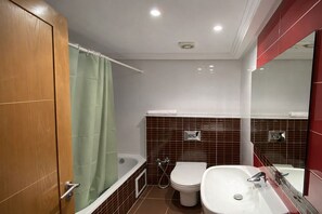 A bathroom with a bathtub, toilet, and sink, featuring a wooden door and a green shower curtain. - Appartement Hannibal (Tunis)