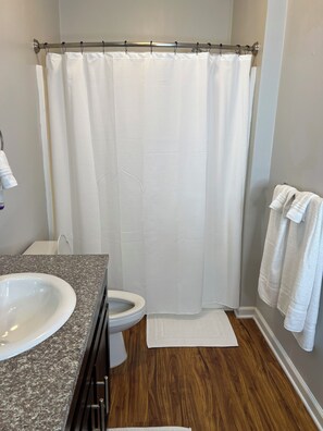 Une salle de bain équipée d’un rideau de douche, de toilettes, d’un lavabo et d’un porte-serviettes.