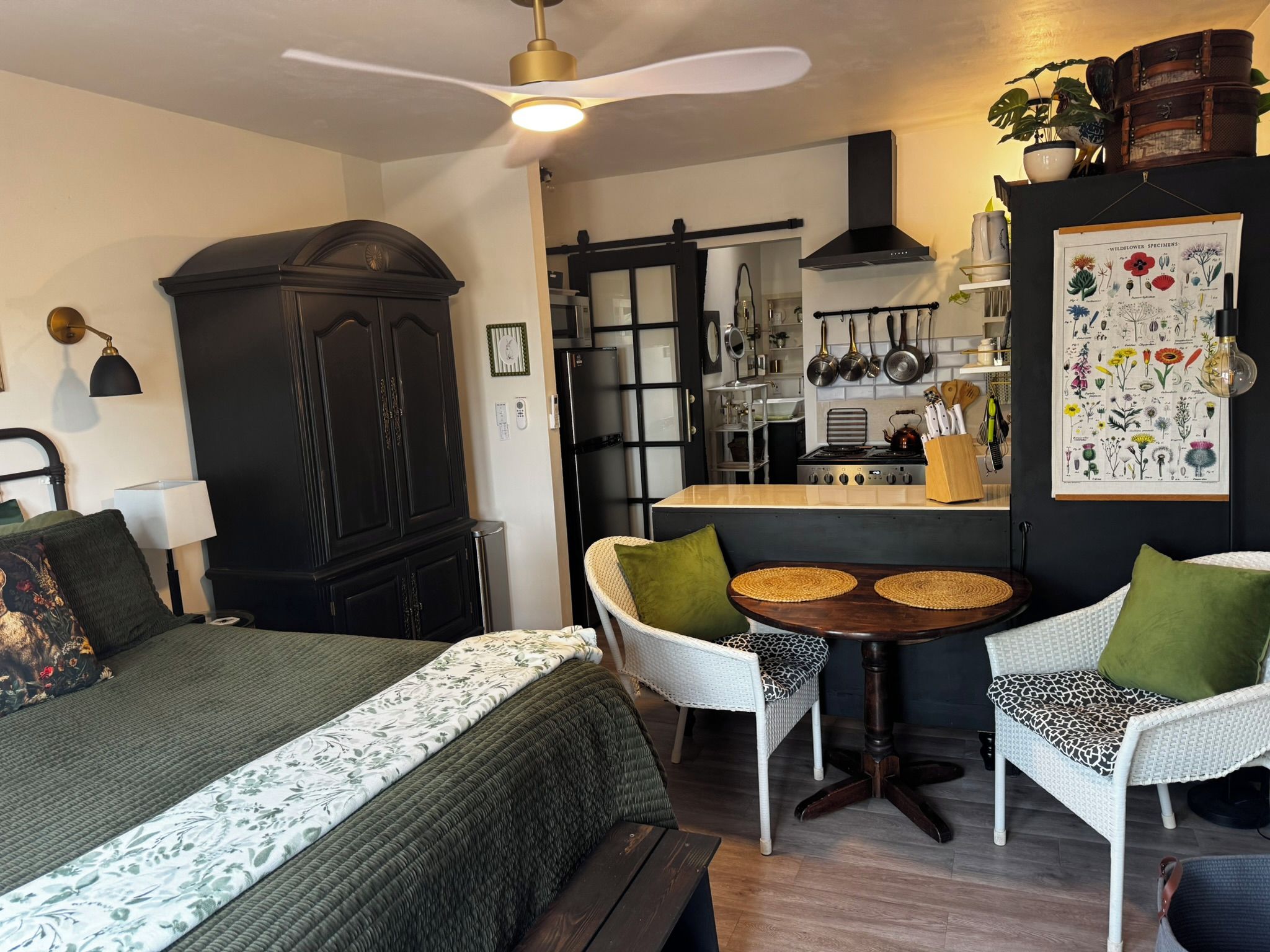 Una habitación compacta con cama, una mesa de comedor con sillas, kitchenette y ventilador de techo.