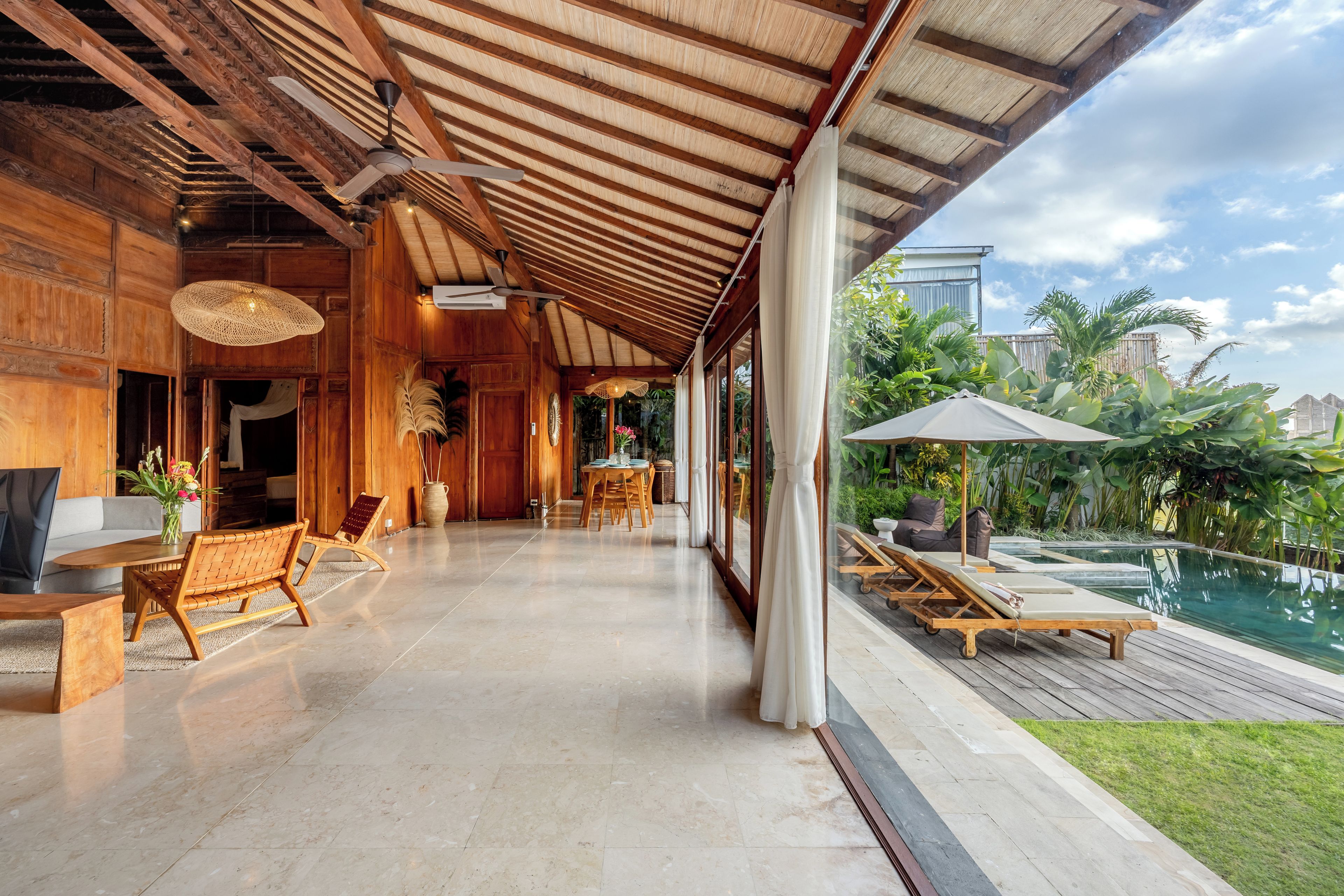 Un espacio exterior cubierto con piscina, mobiliario de madera y vistas al entorno verde.