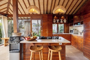 Una cocina con armarios de madera, una isla central con taburetes, una estufa a gas y lámparas colgantes tejidas.