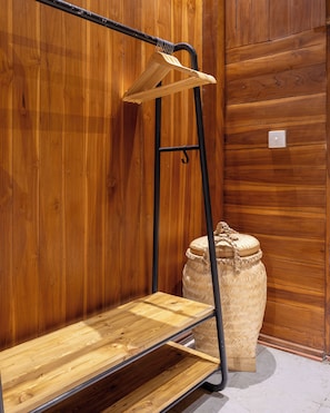 Un banco de madera con estructura metálica, una cesta tejida y una maceta grande tejida frente a una pared de madera.