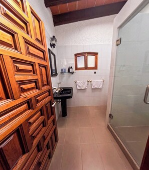 Une salle de bain avec une porte en bois, un lavabo, un miroir, une fenêtre et une douche.