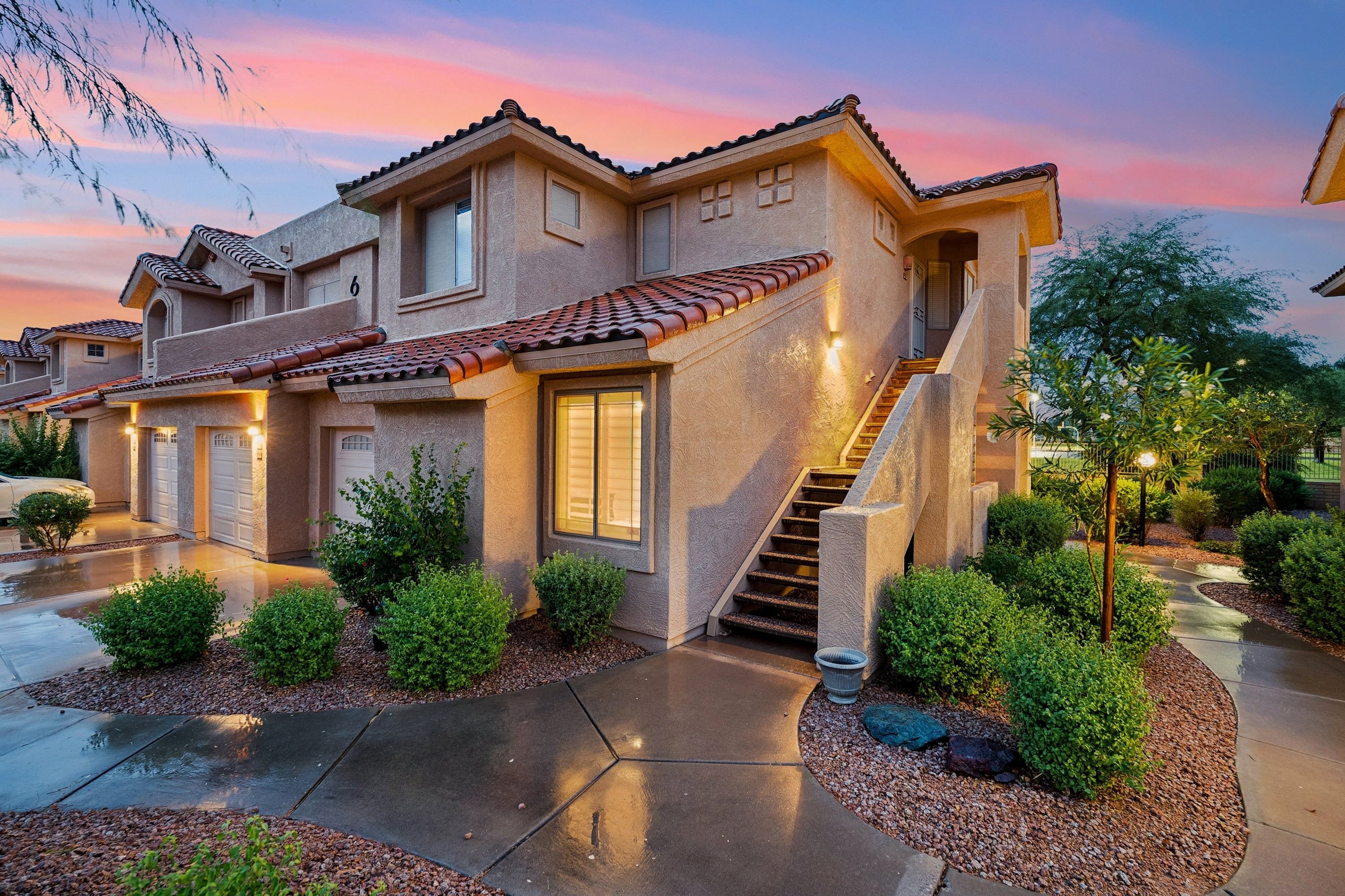 A two-story house with a tiled roof, a front entrance with a staircase, and a driveway.
