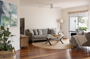 A living room with a grey sofa, a coffee table, a lamp, and a large window. - Oceanic Beach House | Private Pool | Steps to Sand (Sunshine Coast)