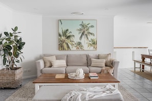 A living room with a sofa, coffee table, and a painting of palm trees. - Oceanic Beach House | Private Pool | Steps to Sand (Sunshine Coast)
