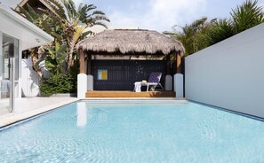 A swimming pool with a thatched-roof structure, a lounge chair, and a small table. - Oceanic Beach House | Private Pool | Steps to Sand (Sunshine Coast)