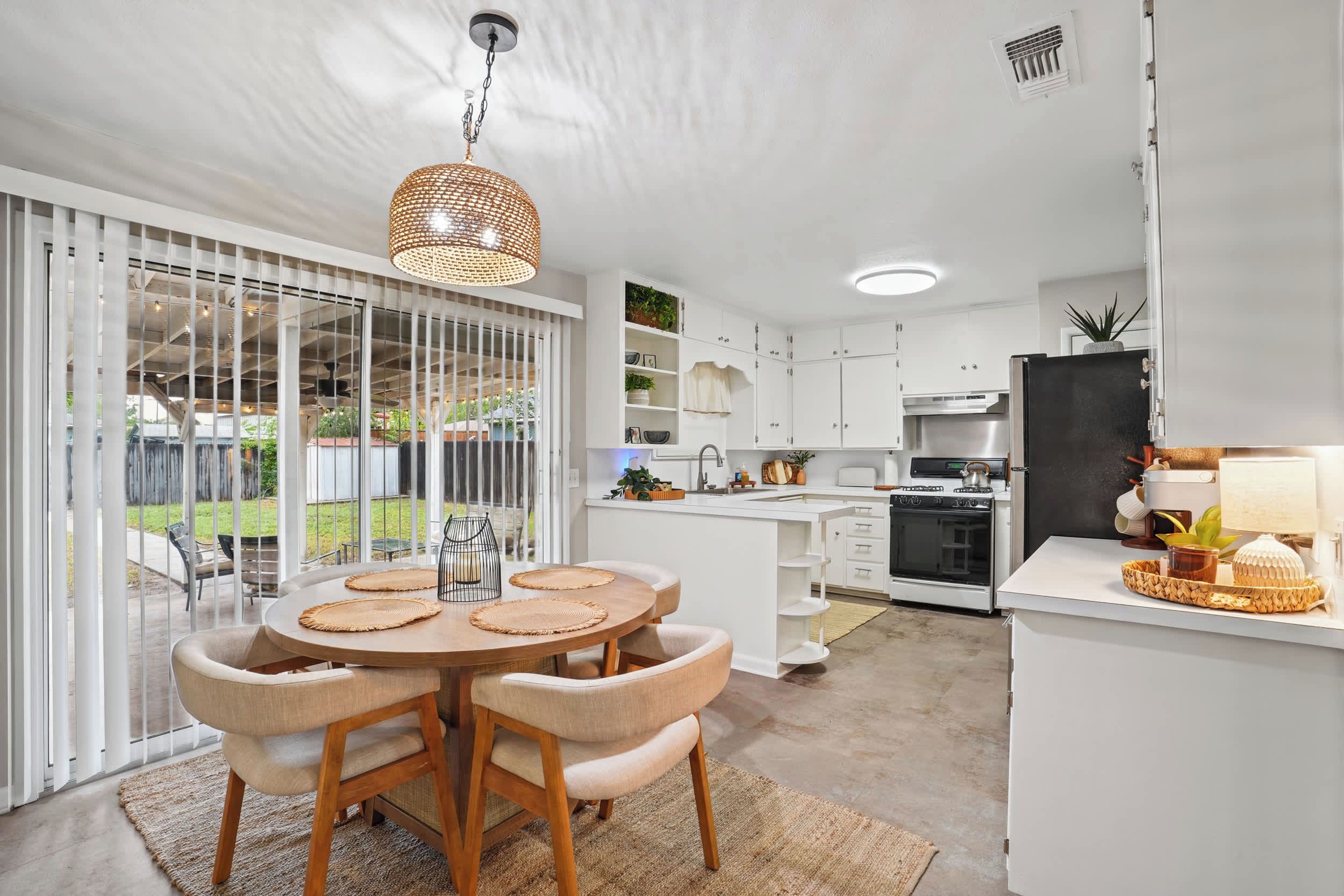 A modern kitchen with white cabinetry, a dining area with a round table and chairs, and a view of the outdoors through large sliding doors.