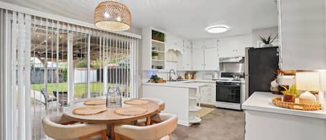 A modern kitchen with white cabinetry, a dining area with a round table and chairs, and a view of the outdoors through large sliding doors.