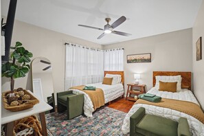 A hotel room with two single beds, a desk, a chair, a small table, a floor lamp, a ceiling fan, and a window with curtains. - Ginger Sol - 2BR/1BA - Centrally Located (Lubbock)