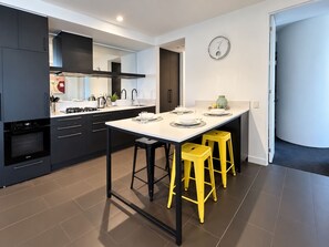 A modern kitchen with a central island, black cabinets, and yellow stools. - Southbank Stunner with 2 Carparks and Dream Views (South Melbourne)