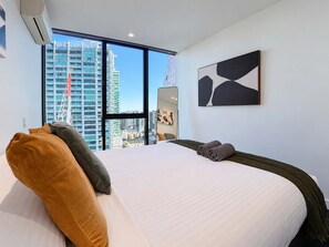Ein Hotelzimmer mit einem großen Bett, Blick auf eine Stadtlandschaft und einem modernen, abstrakten Gemälde an der Wand.