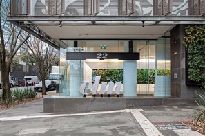 A building entrance with a large glass facade, a metal canopy, and the number 22 above the entrance. - Southbank Stunner with 2 Carparks and Dream Views (South Melbourne)