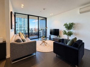 A modern living room with a sofa, a TV, and a plant. - Southbank Stunner with 2 Carparks and Dream Views (South Melbourne)