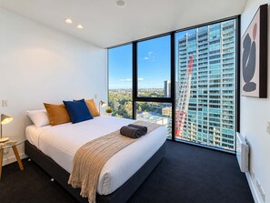 A modern bedroom with a large bed, a view of a cityscape, and a crane outside the window. - Southbank Stunner with 2 Carparks and Dream Views (South Melbourne)