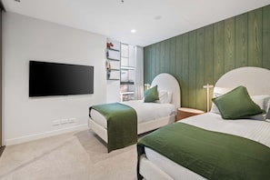 A hotel room with two beds, a flat-screen TV mounted on the wall, and a bookshelf. - Jaw-dropping 4BD Penthouse in Beachside Resort (Port Melbourne)