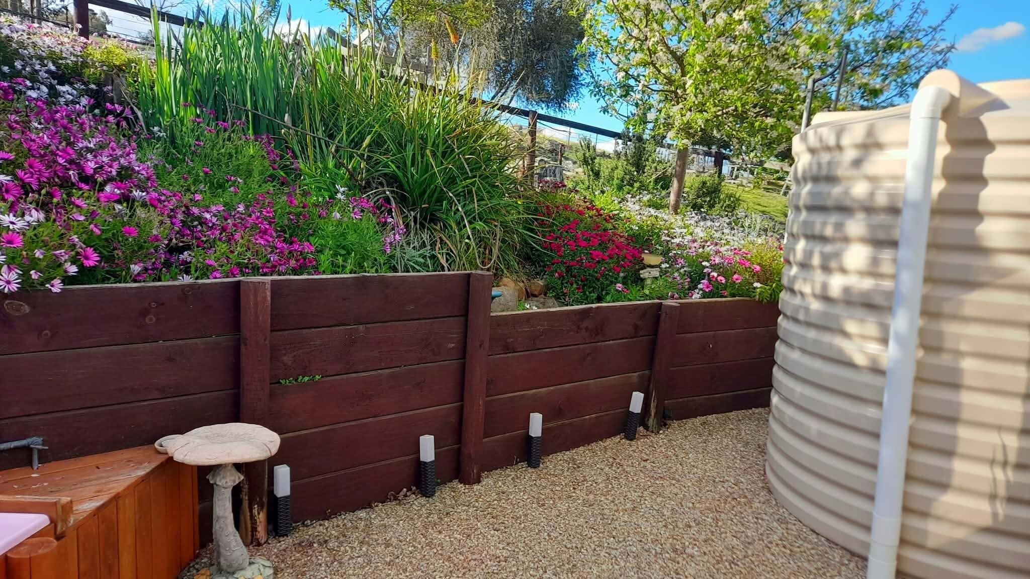 A garden with a wooden fence, a wooden bench, and a water feature.