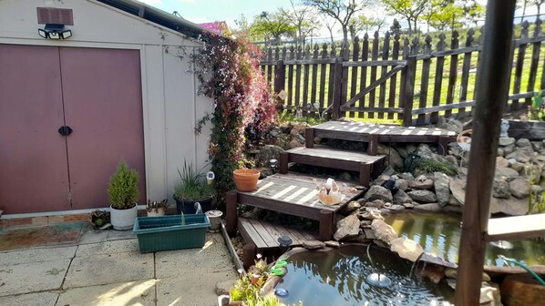 A backyard with a wooden deck, a small pond, and a shed.