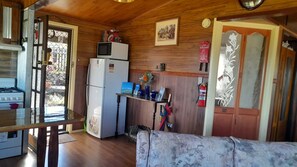 A compact kitchen with a refrigerator, microwave, and stove. There's a small table with a laptop and decorative items. A fire extinguisher is mounted on the wall. - Clives Manor is a cosy cabin nestled in the hills of Turondale. (Turondale)