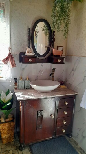 Ein Badezimmer mit Marmorwaschbecken, einem Holzschranken und einem Spiegel, sowie einer hängenden Pflanze.