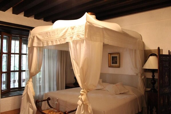 Une chambre à coucher avec un lit à baldaquin, une table de chevet, une lampe et une fenêtre avec des rideaux.
