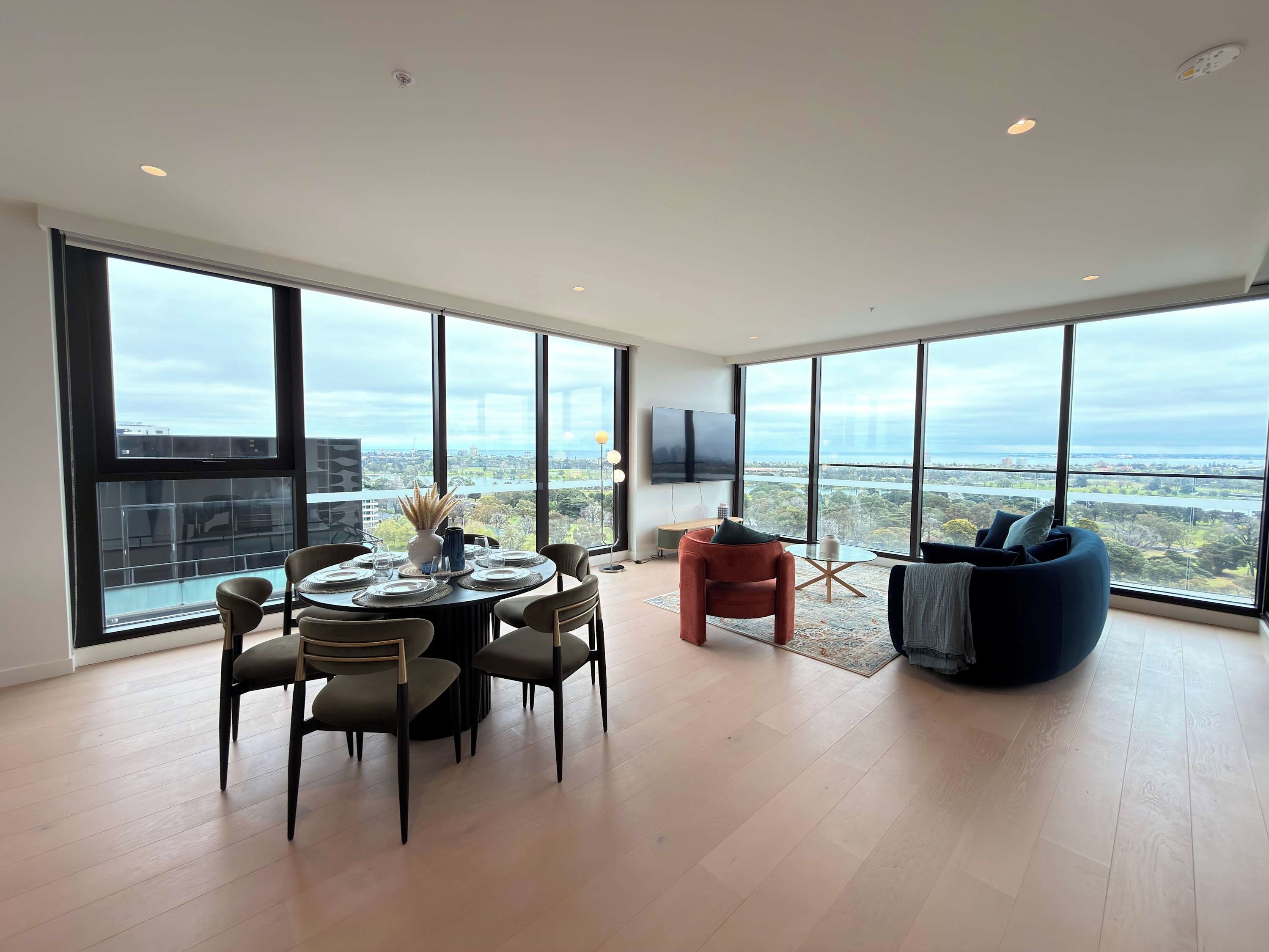 Uma sala de estar moderna com área de jantar, janelas amplas, TV de tela plana e vista para o horizonte da cidade.