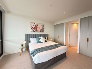 Une chambre moderne avec un grand lit, une table de chevet avec une lampe, un élément décoratif mural et une armoire.