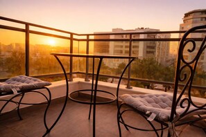 A balcony with a table and two cushioned chairs, overlooking a cityscape during sunset. - Loft italiano (Tunis)
