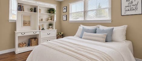 A bedroom with a bed, a white dresser, and a window with blinds.