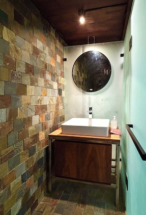 Un bagno con parete in pietra, specchio rotondo e mobile bagno in legno.
