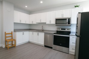 A modern kitchen with white cabinets, stainless steel appliances, and a wooden chair. - 3-bedroom work trip;mid-term;long- term; relocation (Hamilton)