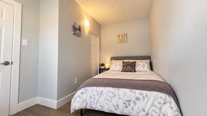 A bedroom with a bed, a door, a nightstand with a lamp, and wall art. - 3-bedroom work trip;mid-term;long- term; relocation (Hamilton)