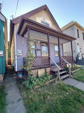 A two-story house with a front porch, a small garden, and a visible electrical box. - 3-bedroom work trip;mid-term;long- term; relocation (Hamilton)