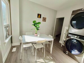 A compact kitchen with a built-in washer and dryer, a dining table with chairs, and a potted plant. - 3-bedroom work trip;mid-term;long- term; relocation (Hamilton)