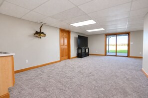 A spacious room with a carpeted floor, a wooden door, a black entertainment unit, and a large window with a view.
