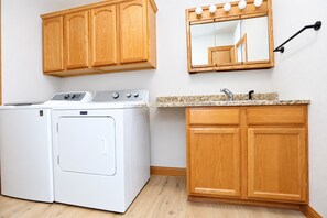 A laundry area with a washer and dryer, wooden cabinets, a granite countertop, and a mirror.