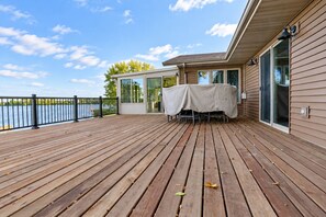 Une terrasse en bois avec une table et des chaises, donnant sur une étendue d’eau.