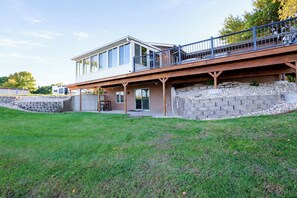 A modern two-story house with a covered patio, a stone retaining wall, and a grassy yard.
