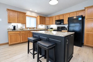A kitchen with wooden cabinets, a black refrigerator, a granite countertop, and two bar stools.