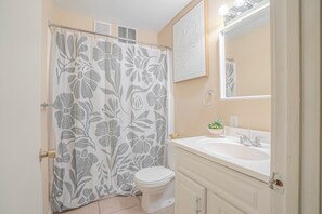 Un baño con inodoro, lavamanos, espejo y cortina de ducha estampada con flores.