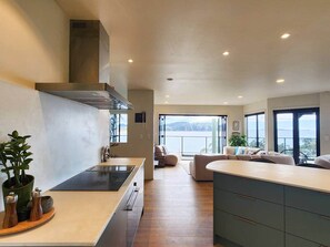 Eine moderne Küche mit einer zentralen Kochinsel, einem Essbereich mit einer Couch und Blick ins Freie.