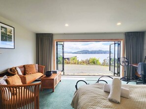 Ein Hotelzimmer mit einer großen Schiebeglastür, die auf einen Balkon führt, einem Sofa, einem Bett und einem kleinen Tisch mit einem Ventilator.