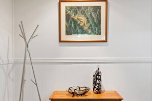 A framed artwork of a frog on a wall, a metal sculpture, and a wooden table with a glass bowl and a vase. - Windsong at Ravensbourne Escape 2 Bedrooms (Ravensbourne)
