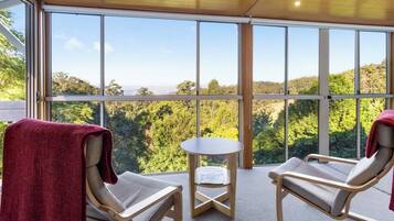 Une pièce comprenant deux fauteuils confortables, une petite table et de grandes fenêtres donnant sur un paysage boisé.