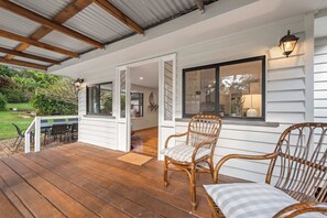 A covered porch with wooden flooring, two wicker chairs, and a table. - Mahali House - 6 Bedroom Holiday House (Ravensbourne)