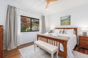 A bedroom with a wooden bed, a bench, a nightstand, a lamp, and a painting on the wall. - Mahali House - 6 Bedroom Holiday House (Ravensbourne)