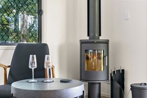 A modern room with a wood-burning stove, a round table with two glasses, and a chair. - Yume House Stylish Country Escape 1 Bedroom (Ravensbourne)