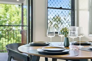 A dining table set with plates and glasses, a vase with a plant, and a view of greenery through a window. - Yume House Stylish Country Escape 1 Bedroom (Ravensbourne)