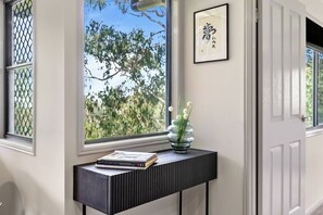A room with a window, a framed picture on the wall, and a small table with a vase and books. - Yume House Stylish Country Escape 1 Bedroom (Ravensbourne)